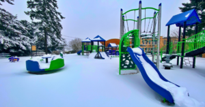 public playground with blue and green equipment in the snow in need of winter playground safety