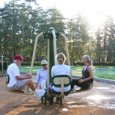 four adults sitting on a piece of outdoor fitness equipment