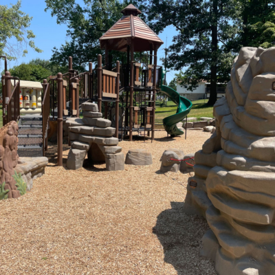 brown and green playground with decorative plastic rocks and tree stumps
